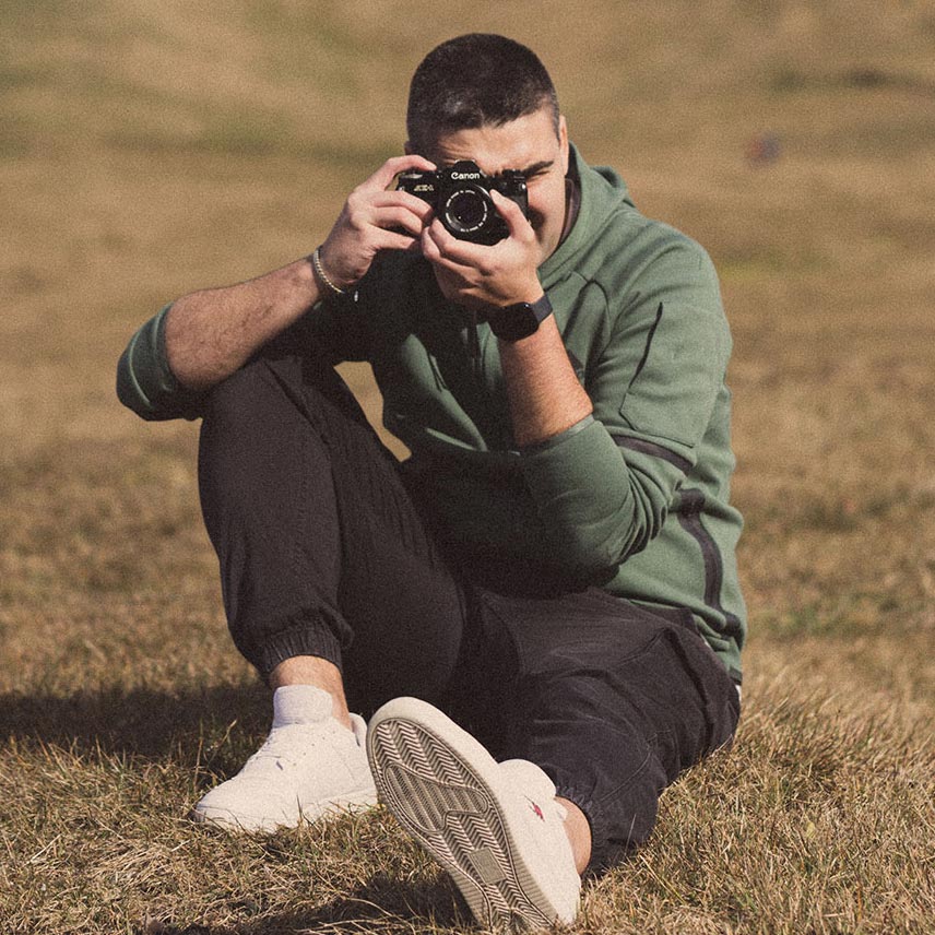 Portrait of Bastian holding a analogue camera in a grassy field